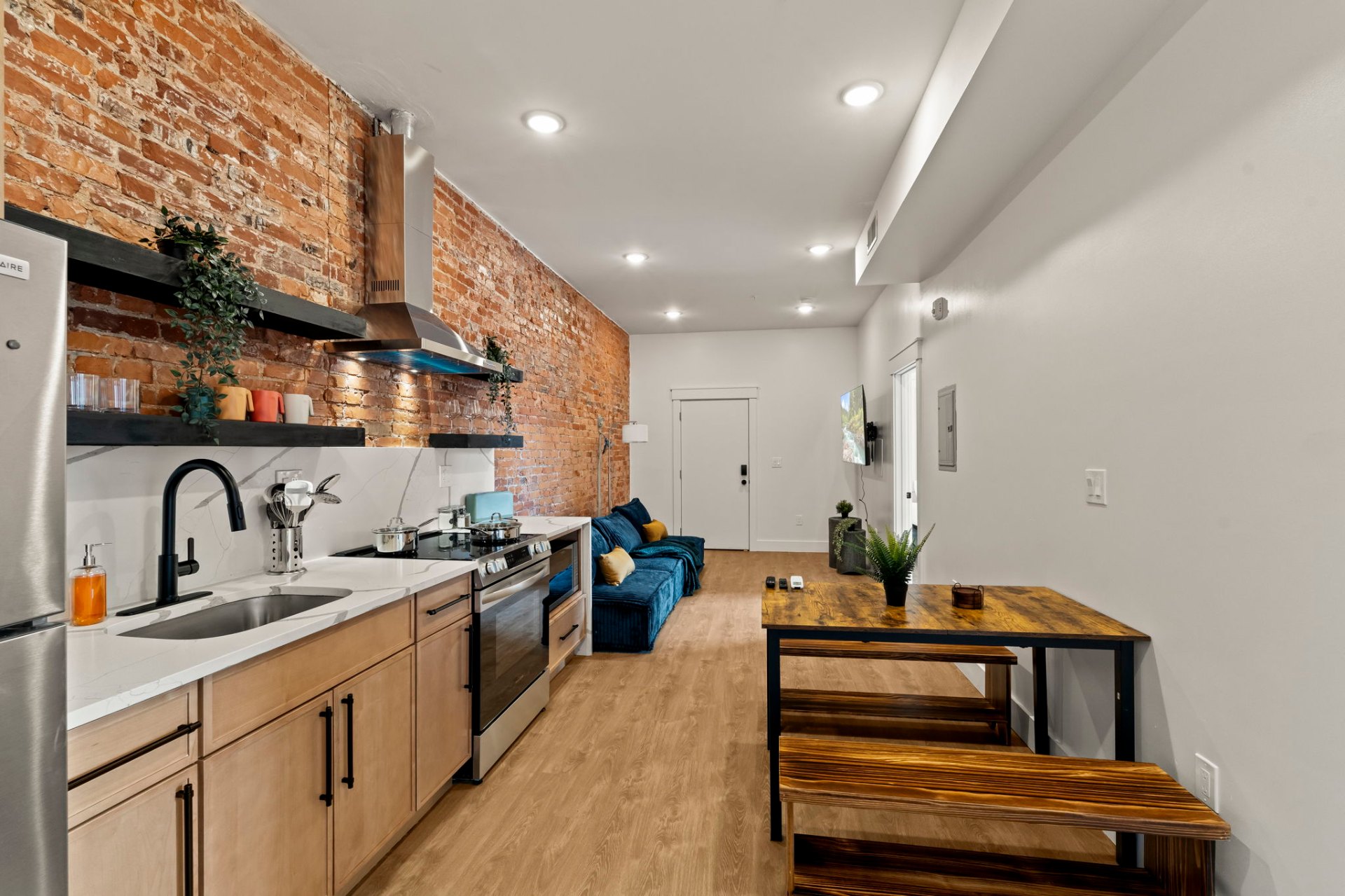 Galley kitchen with exposed brick wall, black shelving and blue sofa
